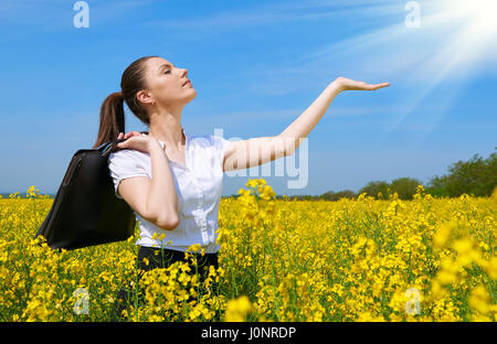 Business Woman with briefcase montrer à sun palm. Jeune fille en fleur jaune champ. Beau paysage de printemps, journée ensoleillée, le colza Banque D'Images