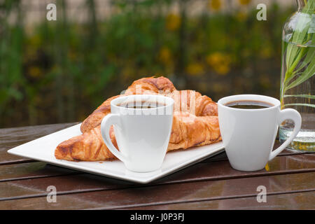 Deux tasses de café et deux croissants sur une table en bois, à l'extérieur Banque D'Images