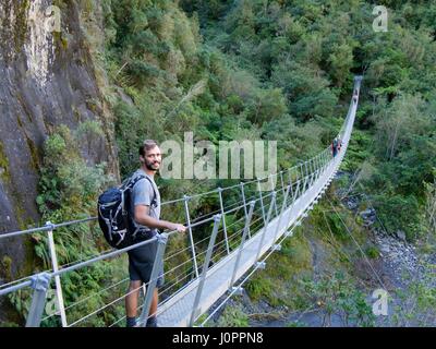 Young male hiker debout sur pont tournant sur des paysages forestiers montagneux Banque D'Images