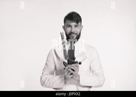 Studio shot of a happy young chef barbu tenant des couteaux sur fond blanc. Chef avec couteau. Handsome smiling cheef détenant plusieurs couteaux tranchants Banque D'Images