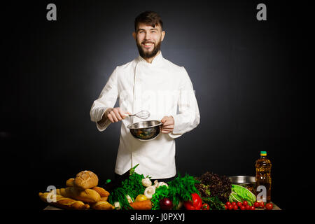 Chef cuisinier avec légumes splah noir et fond noir. L'harmonie musicale. Chef jonglant avec les légumes et autres aliments dans la cuisine. Banque D'Images