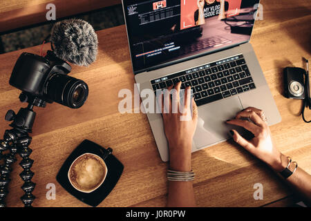 Vue de dessus du montage vidéo vlogger femelle ordinateur portable. Jeune femme travaillant sur ordinateur avec un café et des caméras sur table. Banque D'Images