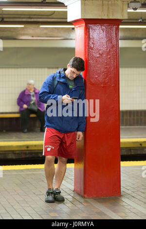 Un jeune homme vérifie son téléphone dans l'attente d'un train Banque D'Images
