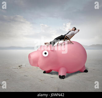 Businessman relaxing on top of piggy bank Banque D'Images