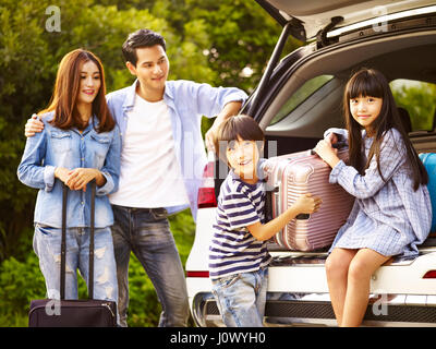 Cute asian enfants aidant décharger les bagages du coffre tandis que les parents regardant affectueusement. Banque D'Images