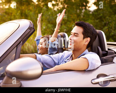 Young Asian couple riding dans un cabriolet sport car au coucher du soleil. Banque D'Images