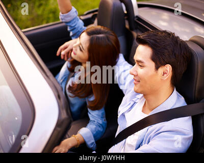 Young Asian couple riding dans un cabriolet sport car au coucher du soleil, high angle view. Banque D'Images