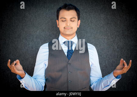 Closeup portrait of handsome, jeune homme en veste et cravate dans la méditation mode zen, fond noir gris isolé. les techniques de soulagement du stress concept. Banque D'Images