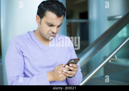 Closeup portrait, a souligné jeune homme en mauve pull, choqué, surpris, horrifié par ce qu'il a troublé voit sur son téléphone cellulaire, de l'intérieur isolé Banque D'Images