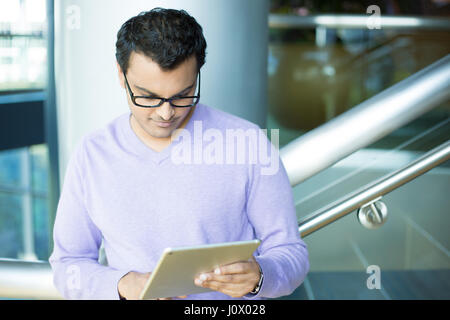 Closeup portrait, jeune captivé, absorbé, absorbé dans l'homme chandail mauve et noir lunettes feuilletant des e-mails, de méditer sur la tablette gris argent t Banque D'Images