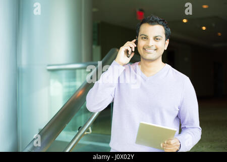 Closeup portrait, beau jeune homme d'affaires, heureux guy, en violet pull, à l'aide de téléphone portable et tablette, souriant, avoir une conversation agréable, isola Banque D'Images