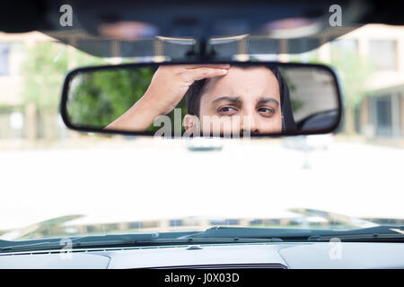 Closeup portrait drôles, jeune homme à la recherche du pilote à l'arrière, rétroviseur intérieur à la perte de cheveux au sommet de veuve questions ou de l'inquiétude, de l'intérieur windsh isolés Banque D'Images