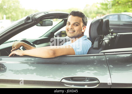 Closeup portrait, happy young smiling man in blue polo shirt noir dans sa nouvelle voiture de sport, détente, looking at camera, isolé sur fond de plein air Banque D'Images