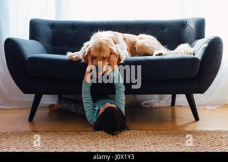 Girl lying sous canapé jouant avec son chien Banque D'Images