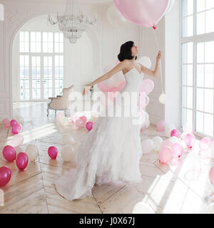 Jeune femme en robe de mariée dans l'intérieur de luxe vole sur ballons rose et blanc. Banque D'Images