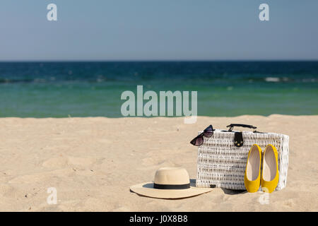 Vacances d'été en mer. Valise en osier blanc et des accessoires féminins et des chaussures sur la plage. Focus sélectif. Banque D'Images