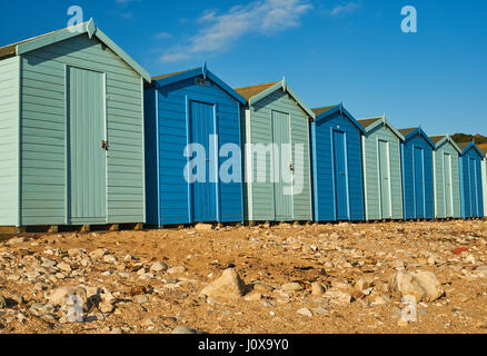 Charmouth, Dorset et une ligne de cabines de plage en alternant les couleurs bleu clair et foncé à l'arrière de la plage de galets sur un soir d'été. Banque D'Images