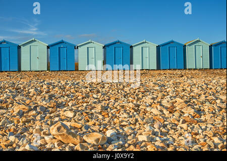 Charmouth, Dorset et une ligne de cabines de plage en alternant les couleurs bleu clair et foncé à l'arrière de la plage de galets sur un soir d'été. Banque D'Images