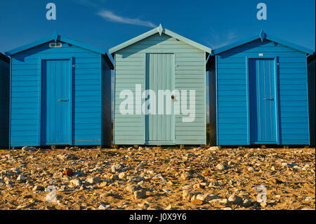 Charmouth, Dorset et une ligne de cabines de plage en alternant les couleurs bleu clair et foncé à l'arrière de la plage de galets sur un soir d'été. Banque D'Images