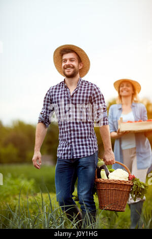 Cheerful couple agriculteurs revenant de jardin avec produits végétariens Banque D'Images