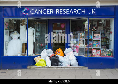 Cancer Research UK avant de boutique avec des sacs en plastique remplis de dons. Banque D'Images