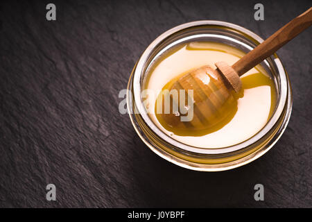 Cuillère dans un bol de miel sur une ardoise foncé Banque D'Images