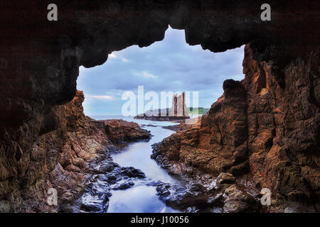 Petite grotte rocheuse face à la formation de roches Cathédrale Kiama au coucher du soleil. La côte de grès colorés érodées par l'océan Pacifique au fil des ans. Banque D'Images