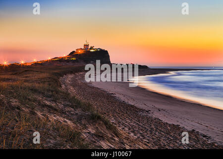 Avec l'herbe des dunes de sable à la plage de Nobbys nobbys head, et phare de Nobbys à Newcastle, NSW, au lever du soleil orange colorés. Banque D'Images