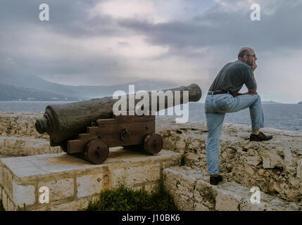 Korcula, Croatie. 9 octobre, 2004. Debout à côté d'un ancien village médiéval fortifié cannon dans la vieille ville de Korcula, Croatie, un touriste regarde sur les Peljeski Kanal, où plusieurs batailles historiques ont eu lieu, vers le continent. Korcula est devenue une destination touristique internationale. Credit : Arnold Drapkin/ZUMA/Alamy Fil Live News Banque D'Images