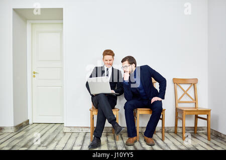 Portrait de deux business people using laptop assis sur des chaises dans la salle d'attente à l'extérieur du bureau Banque D'Images