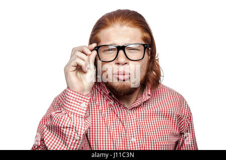 La pensée réfléchie readhead barbu businessman avec chemise rouge et de rousseur holding glasses and looking at camera . studio shot isolé sur blanc. Banque D'Images