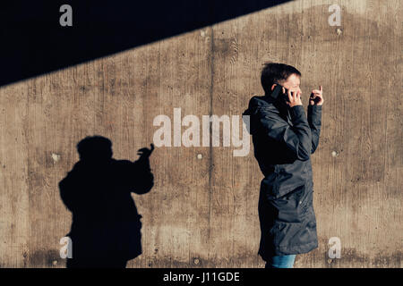 Authentique sérieux femme avec cheveux courts talking on mobile phone sur la rue dans le passage sous l'hiver, Soleil couchant casting shadows contrastée sur th Banque D'Images