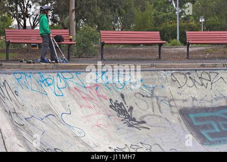 Trois banquettes rouges et un garçon sur un scooter donnant sur un couvert de graffitis half pipe à un skate park. Banque D'Images