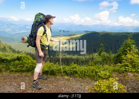 Voyageur avec sac à dos sur le sommet de la montagne. Jeune homme hiker relaxing on au sommet de la montagne et profiter de la vue de la vallée et bleu ciel nuageux. Guérir Banque D'Images