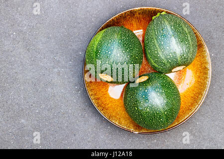 Trois courgettes rondes sur une plaque jaune avec un fond gris et copier l'espace. Banque D'Images