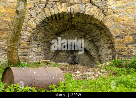 Gros plan d'un ancien four à chaux industriel abandonné surcultivé avec un grand tambour à huile rouillée, Midlothian, Écosse, Royaume-Uni Banque D'Images