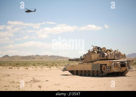 Des soldats américains dans un hélicoptère d'attaque AH-64 Apache, affecté à la 1ère Brigade Combat Team, 3e Division d'infanterie, voler au-delà d'un réservoir d'Abrams, au cours de l'action décisive 17-05 Rotation au Centre National d'entraînement à Fort Irwin, en Californie, Avril 03, 2017. (U.S. Photo de l'armée par la CPS. Sacharok JD, Operations Group, National Training Center) Banque D'Images