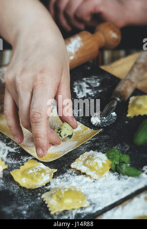 Préparation de raviolis dans la cuisine avec des outils et ingrédients : pâte, farine, œufs, farce, couteau, rouleau, planche. Mettre à la main des pâtes. Banque D'Images