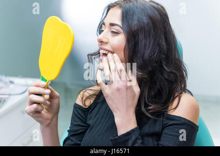 Dame contrôler les dents en miroir. Jeune femme au bureau de dentiste. De nouveaux implants dentaires. Banque D'Images