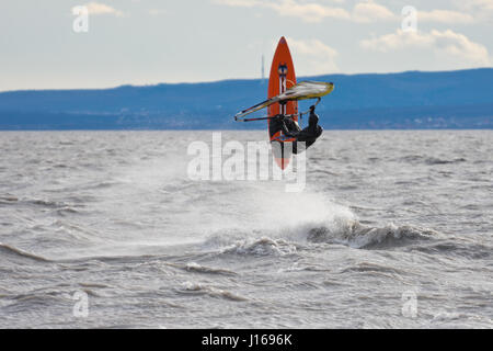 Planche sur le Neusiedlersee (Lac de Neusiedl) d'effectuer un saut dans le vent fort et les vagues. Temps froid, ciel nuageux Banque D'Images