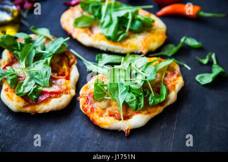 Mini pizzas bruschettas ou avec du fromage, salami et feuilles d'épinards frais Banque D'Images