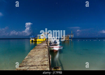 La pleine lune éclaire le ciel nocturne au-dessus d'une jetée en bois branlante à West Bay, Roatan, Honduras. Banque D'Images