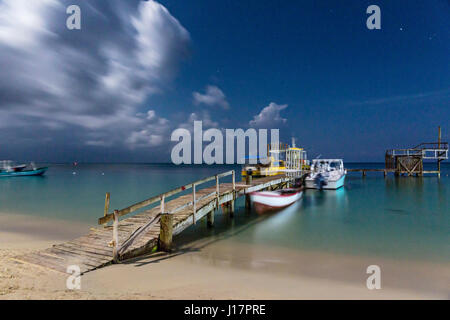 La pleine lune éclaire le ciel nocturne au-dessus d'une jetée en bois branlante à West Bay, Roatan, Honduras. Banque D'Images