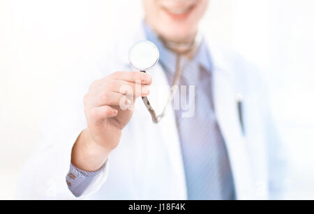 Gros plan d'une main du médecin, la tenue d'un stéthoscope tendus vers l'observateur. Manteau blanc du médecin donne de l'espace pour le côté gauche du châssis. Banque D'Images