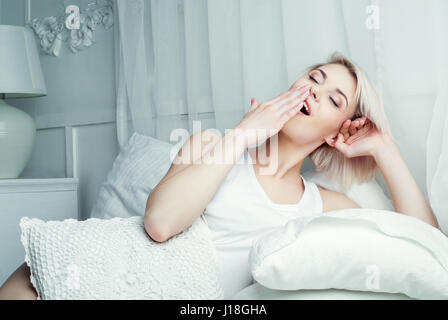 Belle jeune blonde woman yawning in bed at home Banque D'Images