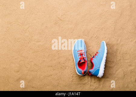 Chaussures de sport bleu avec lacets rose posés sur la plage de sable de background, studio shot, mise à plat. Copier l'espace. Banque D'Images