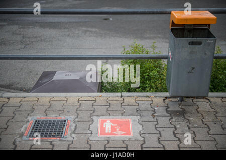 Une cigarette gully à côté d'une poubelle, photographié à un arrêt de bus à Stuttgart, Allemagne, 19 avril 2017. Les fumeurs à Stuttgart sera bientôt en mesure de simplement déposer leurs mégots dans un ravin sur le sol. Les autorités locales de transport font l'essai des contenants en forme de cube à un arrêt d'autobus dans le quartier Vaihingen de Stuttgart. Photo : Lino Mirgeler/dpa Banque D'Images