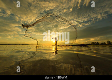 Thai Fisherman sur bateau en bois jetaient un filet pour attraper les poissons d'eau douce dans la rivière de la nature en début de soirée avant le coucher du soleil Banque D'Images