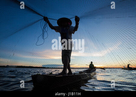 Thai Fisherman sur bateau en bois jetaient un filet pour attraper les poissons d'eau douce dans la rivière de la nature en début de soirée avant le coucher du soleil Banque D'Images