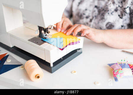 Patchwork et quilt dans l'atelier d'un tailleur femme sur fond blanc - gros plan sur les mains et sur mesure avec machine à coudre des morceaux de tissu bleu et jaune pour patchworking Banque D'Images